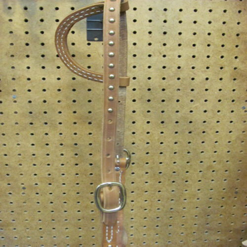 A Big Horn One Ear Brass Stud Headstall hanging on a pegboard.