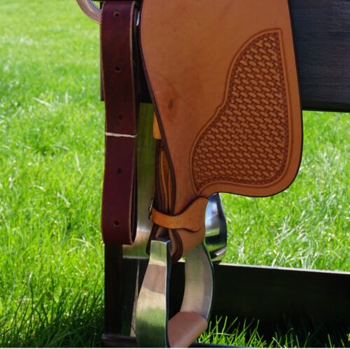 A 16 1/2" Custom Reiner Saddle on a wooden bench in a grassy field.