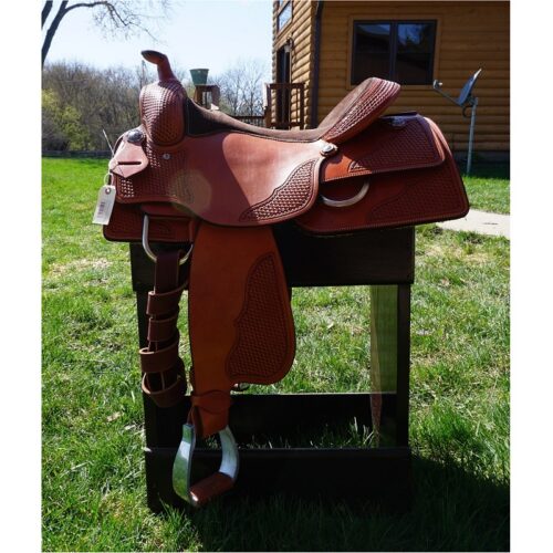 A brown saddle, 16" Custom Square Skirt Reining Saddle, sitting on top of a grassy area.