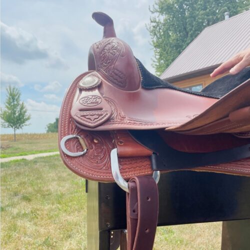 Bob Avila is holding a Bob Avila 16.5" Reining Saddle in front of a barn.